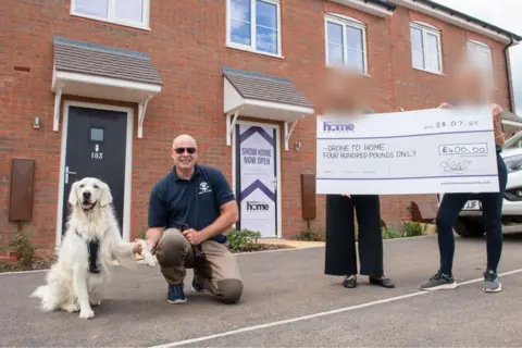Platform Home Ownership Phil James holding hands with a dog and being presented with a cheque for £400
