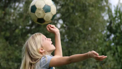 Getty Images Girl heading a football in a park.