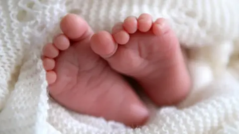PA Media Images showing a new born baby's feet wrapped in a white knitted blanket.