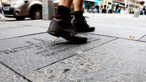 The boots of a person walking on paving slabs in Inverness city centre