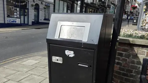 North Yorkshire Council A black bin with a metal opening on a high street.