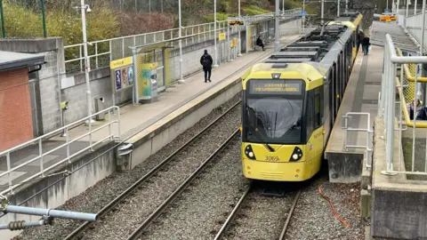 Yellow tram seen next to the platform at West Didsbury station 