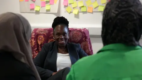 Jacqueline Adusei sat in a chair talking to two refugees with their backs to the camera