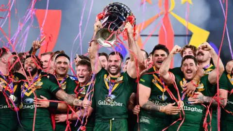 Australia captain James Tedesco lifts the World Cup trophy surrounded by his team-mates after their win over Samoa in the 2021 final at Old Trafford