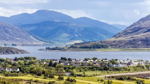 A view over Ullapool, Loch Broom and hills and mountains beyond. It is a sunny day.