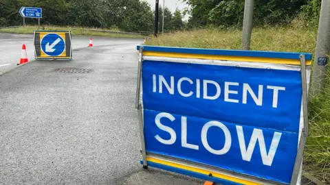 A blue sign which reads 'Incident Slow' which is positioned on the side of the road.