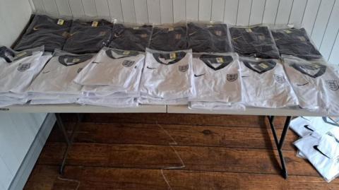 Fake England shifts in packaging laid out on a table after being recovered in a raid