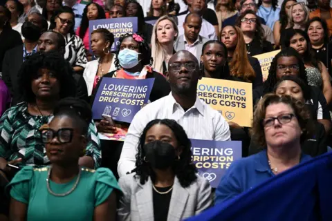 Getty Images People in the crowd hold signs that read "Lowering prescription drug costs"