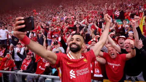 Mo Salah takes a selfie at Anfield with fans cheering in the stand behind