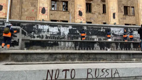 Cleaners remove graffiti from the walls outside the parliament in Georgia