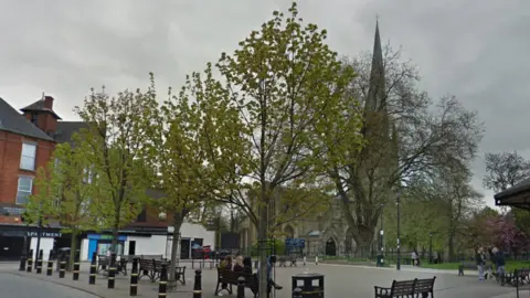 Google A paved area with some trees in front of a church with a crooked spire