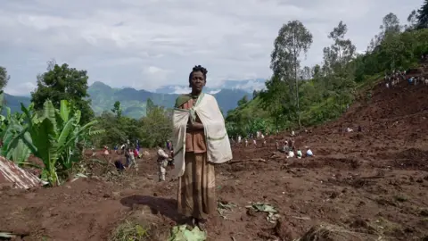 Amnessa Eva/BBC Uma mulher fica na lama resultante de um deslizamento de terra