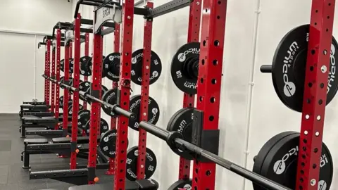 Daniel Wiffin Gym equipment. There are red bars and black weights.