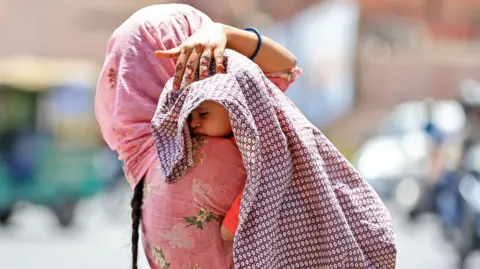 A woman is covering her child to protect from the scorching sun on a hot summer day in Jaipur, Rajasthan, India, on May 25, 2024. 