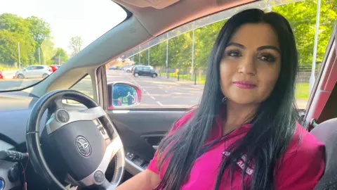 BBC/JULIA LEWIS Amberine Nawaz sitting in the pink taxi, wearing a pink T-shirt