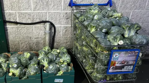 Shepton Mallet Community Fridge A shopping trolley full of broccoli next to green open top food boxes also containing broccoli