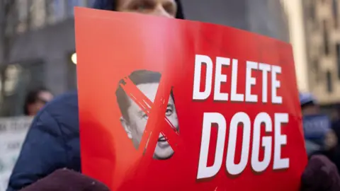 Man holds red sign that reads "Delete Doge"