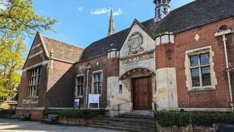 An exterior photo of a old brick building with wooden doors and "public library" carved out of stone above the doors.  