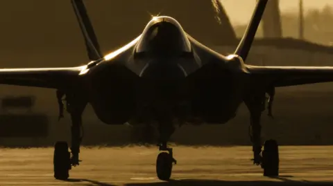 Getty Images The silhouette of an F-35 plane preparing to take off at sunset. The photo is taken head on.