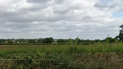 A field beyond a fence, with trees in the distance and grey clouds above