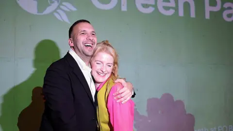 Getty Images Grinning Green Party leader Zack Polanski hugs victorious candidate Hannah Spencer against a Green Party backdrop