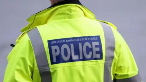 PA Media An officer wears a yellow high-vis jacket with the words Greater Manchester Police on the back.