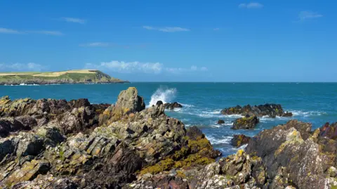 The rugged Solway coastline in southern Scotland with jagged rocks and a green piece of land jutting out into the water