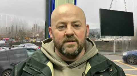 Steve Jones/BBC Pete Narey, who is bald. Narey has dark-coloured facial hair and is wearing a black jacket and brown hoodie.