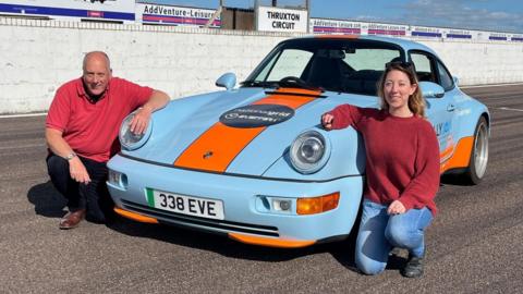 A classic Porsche painted blue and orange with a man and woman knelt on either side