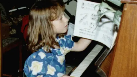 Old photo of a young girl reading sheet music at a piano.