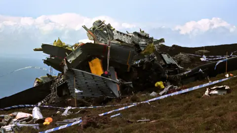 PA Media The wreckage of an aircraft and police tape on a rocky outcrop by the coast