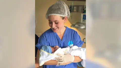 Family handout Emily Oliver in blue nurses clothes holding a baby
