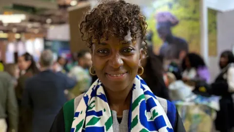 A woman smiling with a scarf on and people in the background