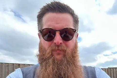 Supplied A head and shoulders photo of a heavily bearded man with glasses
