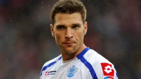 Akos Buzsaky playing in the blue and white hoops of QPR. He has short brown hair.