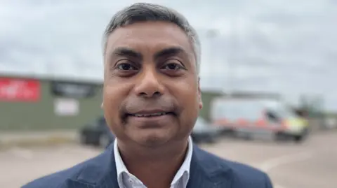 A head and shoulders picture of a man in a jacket and shirt.