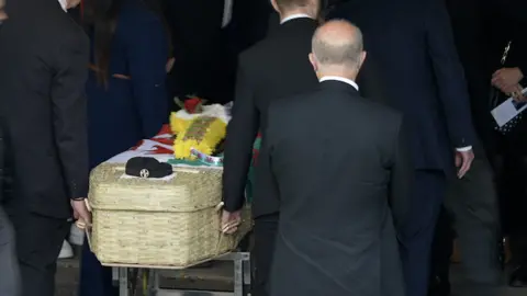 Dewi Morris funeral casket, with his trademark hat and a floral banjo sitting on a Welsh flag on the wicker coffin