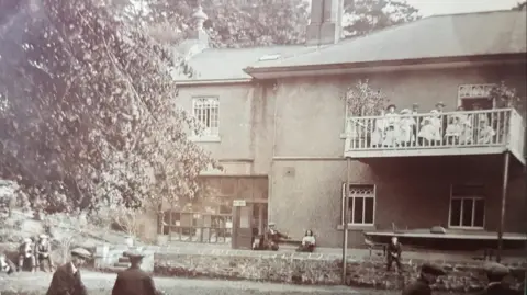 BIRLEY SPA PRESERVATION TRUST Another historic photo of the spa, which shows people sat on an outdoor balcony, with children wearing flat caps sat on the ground below them.
