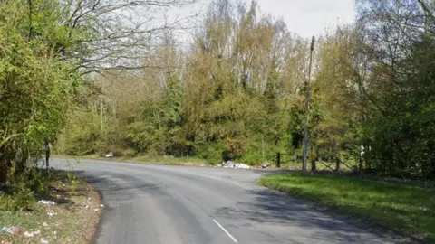 Google A tree-lined road heading into a bend with a gated road to the right