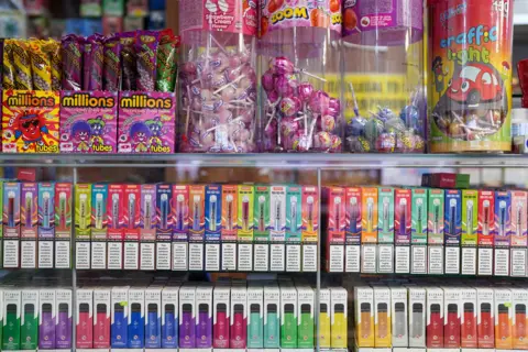 A picture of colourful Vapes in a shop by sweets