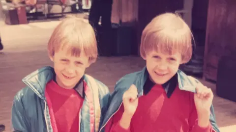 Nick Dawson Two boys wearing red jumpers with black collars. They are smiling at the camera.