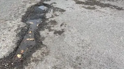Derek Bennett Pothole: a black damp pothole on a grey road