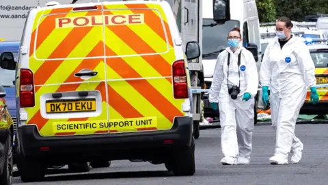 PA Media Police Scientific Support Unit van and two female police officers in blue masks and white hazmat suits