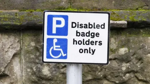 A sign with the words 'Disabled badge holders only' on, in front of a stone wall. 