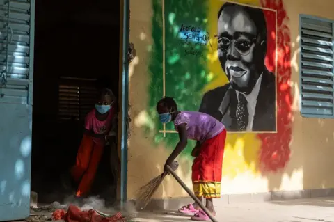 JEROME FAVRE / EPA Children sweep the floor at Medina Gounass Elementary School. On the wall is a mural of the country's first president, Léopold Sédar Senghor.