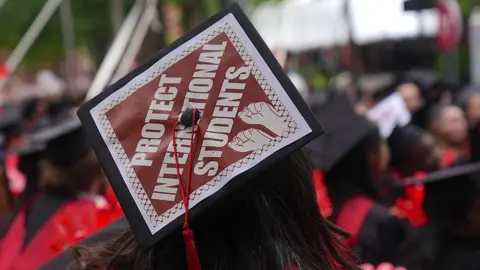 A Harvard University graduate wearing a hat that says "protect international students" during a graduation ceremony at Harvard in Cambridge, Massachusetts on 29 May 2025.