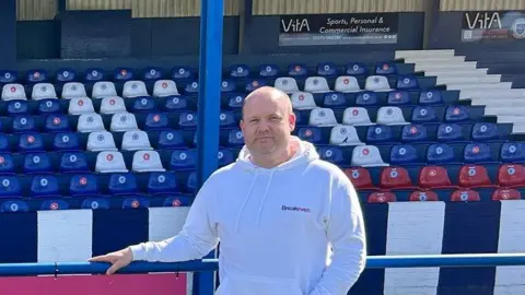 Breakeven Dan Chandler with a hoodie and jeans stood in a football stadium