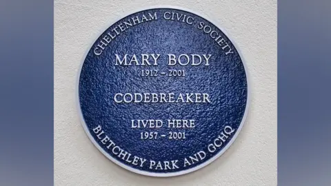 Cheltenham Civic Society A blue plaque on a white exterior wall. It reads "Cheltenham Civic Society. Mary Body. 1912 to 2001. Codebreaker. Lived here 1957 to 2001. Bletchley Park and GCHQ"