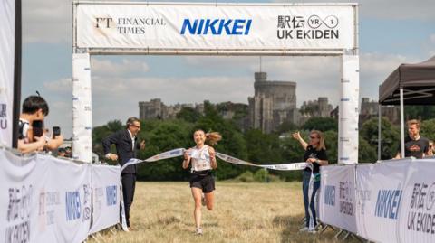 University of Oxford runner Josephine Auer crosses the finish line at Windsor, with Windsor Castle at the background and representatives of UK and Japanese media on the sides