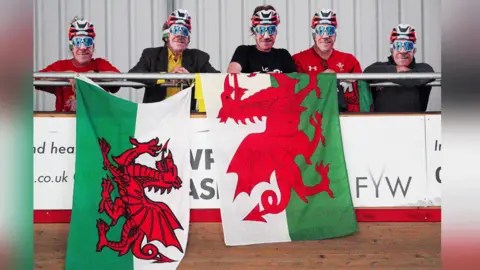 PA Media Five fans wearing Geraint Thomas face masks, they hold two Wales flags in front of them. 